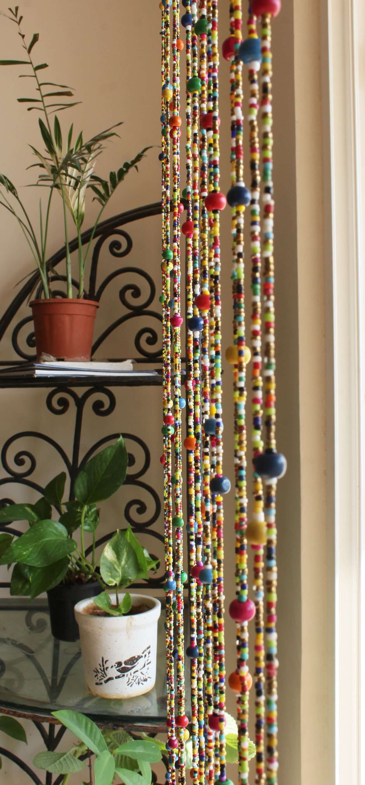 Colorful bohemian beaded doorway garland with jingle bells hanging near plants in a home setting.